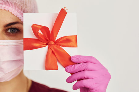 Young female dentist in uniform standing in stomatology office and holding paper with gift length in...