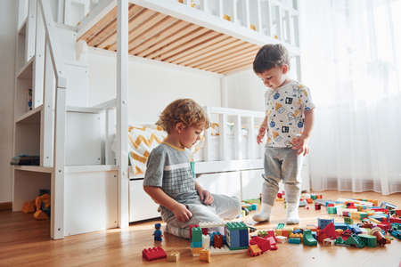 Two little boys have fun indoors in the bedroom with plastic construction set.の写真素材
