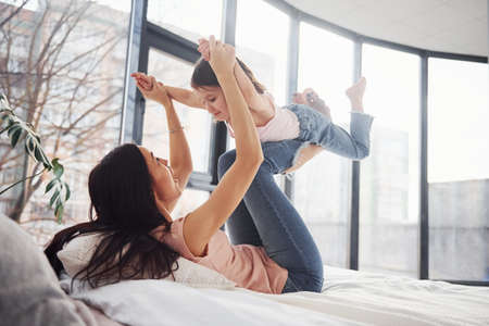 Young mother with her daughter spending weekend together on bed.の写真素材