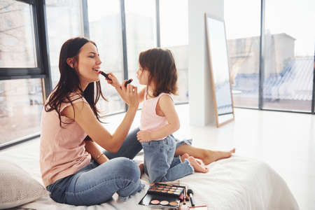 Learning how to make up. Young mother with her daughter spending weekend together in room.の写真素材