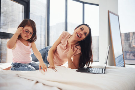 Young mother with her daughter spending weekend together in room and using laptop.