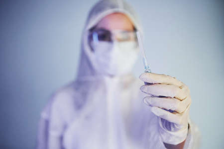 Holds syringe. Portrait of female doctor scientist in lab coat, defensive eyewear and mask.の写真素材