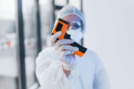 Holds infrared thermometer. Portrait of female doctor scientist in lab coat, defensive eyewear and mask.の写真素材