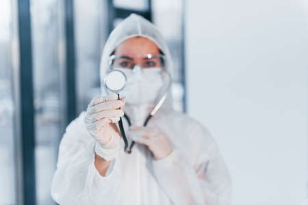 With stethoscope. Portrait of female doctor scientist in lab coat, defensive eyewear and mask.の写真素材