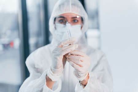 Holds syringe. Portrait of female doctor scientist in lab coat, defensive eyewear and mask.の写真素材