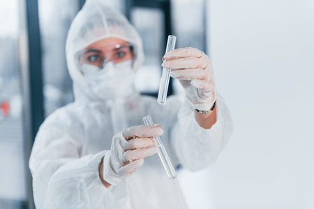 Holds test tubes. Portrait of female doctor scientist in lab coat, defensive eyewear and mask.