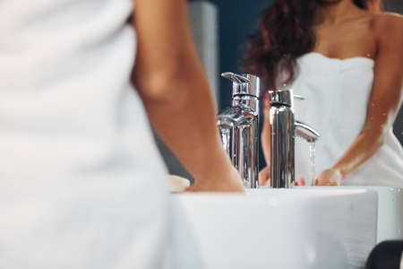 Beautiful brunette standing in bathroom near the mirror and washing hands.の写真素材