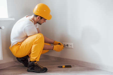 Handyman in yellow uniform works with electricity and installing new socket. House renovation conception.の写真素材