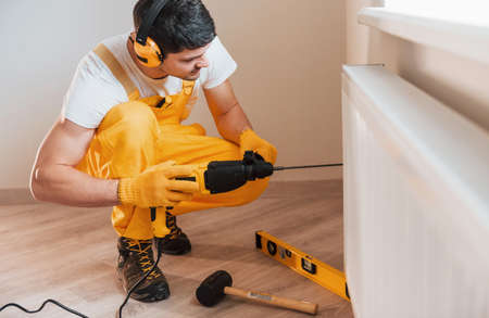 Handyman in yellow uniform works indoors by using hammer drill. House renovation concept.の写真素材