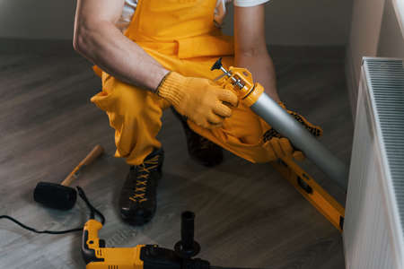 Handyman in yellow uniform works indoors with heat battery by using special tool. House renovation concept.の写真素材