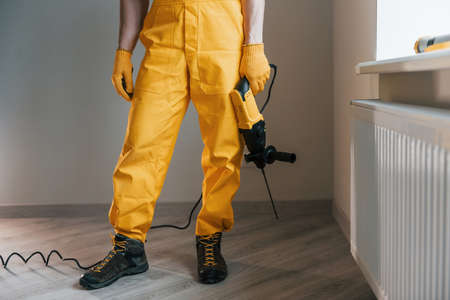 Handyman in yellow uniform with drill standing indoors. House renovation concept.の写真素材
