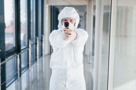 Female doctor scientist in lab coat, defensive eyewear and mask standing indoors with infrated...