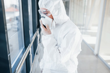 Female doctor scientist in lab coat, defensive eyewear and mask standing indoors.