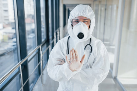 Stop the virus gesture. Female doctor scientist in lab coat, defensive eyewear and mask standing...