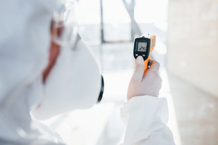 Female doctor scientist in lab coat, defensive eyewear and mask standing indoors with infrated...