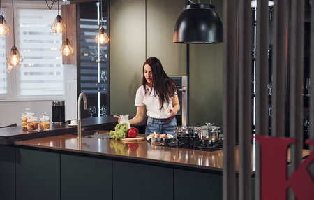 Young beautiful brunette in casual clothes preparing healthy food in kitchen at daytime.