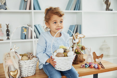 Cute little girl celebrating Easter holidays indoors holding basket with eggs.