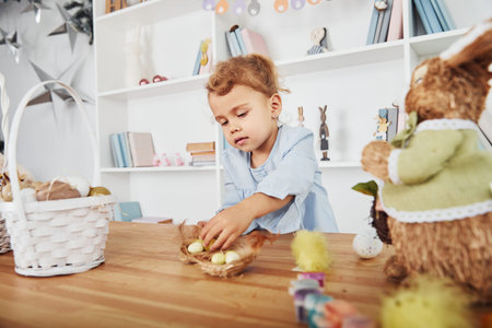 Cute little girl celebrating Easter holidays indoors near table with eggs.