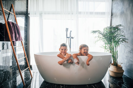 Two kids having fun and washing themselves in the bath at home. Posing for a cameraの写真素材