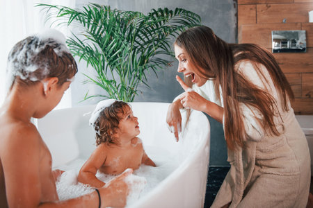 Having fun. Young mother helps her son and daughter. Two kids washing in the bathの写真素材