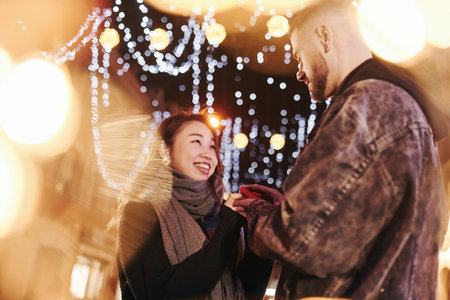 Guy doing proposal. Happy multiracial couple together outdoors in the city celebrating New yearの写真素材