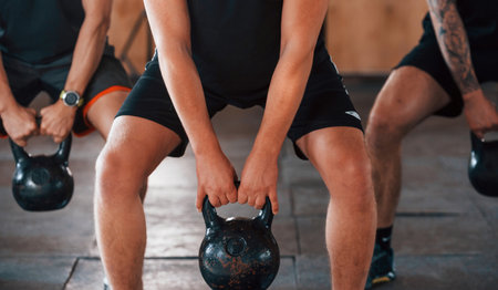 By using heavy weights. Group of young sportive people have crossfit day indoors in gymの写真素材