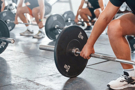 By using heavy weights. Group of young sportive people have crossfit day indoors in gymの写真素材
