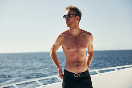 In sunglasses. Young male tourist is on the yacht on the sea. Conception of vacationの写真素材
