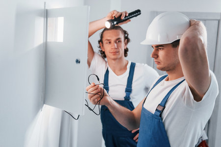 Two young male electricians works indoors together. Using flashlightの写真素材
