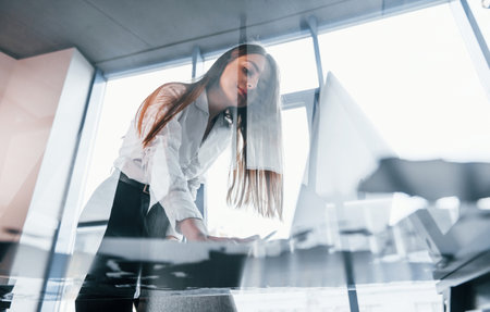 View from below. Young woman in white formal clothes is indoors in the modern officeの写真素材