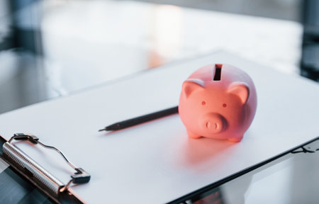 Close up view of pink piggy bank that lying on the white document on tableの写真素材