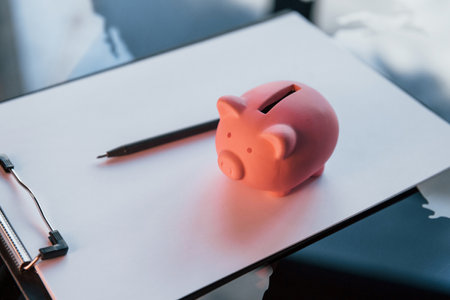 Close up view of pink piggy bank that lying on the white document on tableの写真素材