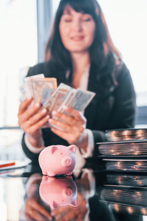 With currency. Woman in black formal clothes is indoors in the modern officeの写真素材