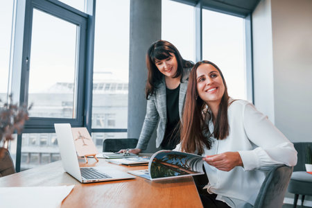 Two women in formal clothes is indoors in the modern office works togetherの写真素材