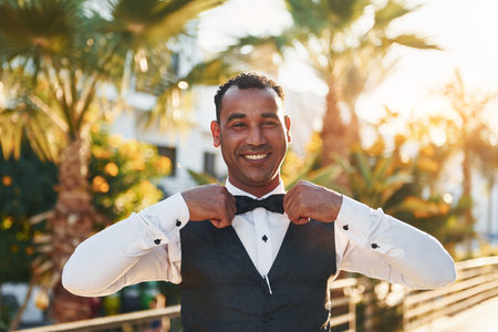 Posing for a camera. Black waiter in formal clothes is at his work outdoors at sunny daytime