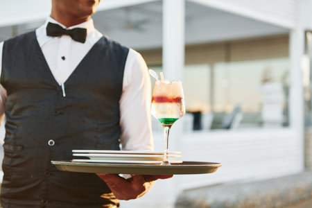 Close up view of drink. Black waiter in formal clothes is at his work outdoors at sunny daytimeの写真素材