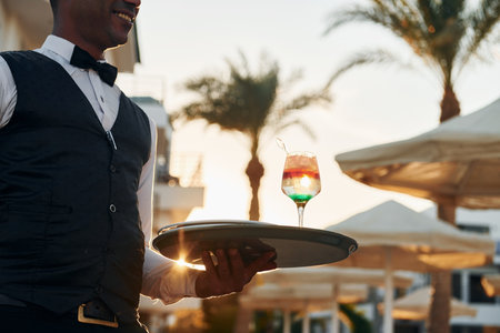 Close up view of drink. Black waiter in formal clothes is at his work outdoors at sunny daytimeの写真素材
