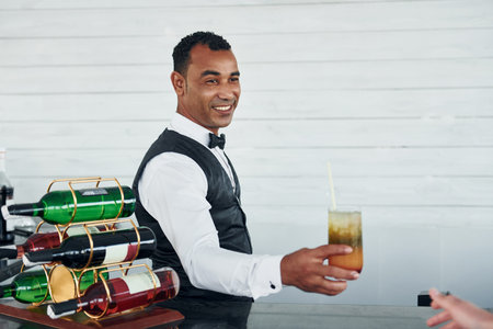With order in hand. Black waiter in formal clothes is at his work outdoors at sunny daytimeの写真素材