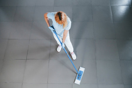 Top view of woman in blue shirt and protective gloves that uses vacuum cleanerの写真素材