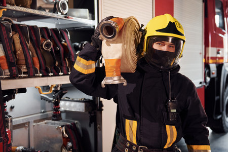 Holds hose. Male firefighter in protective uniform standing near truckの写真素材