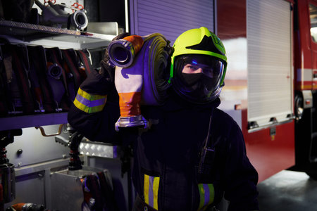 Holds hose. Male firefighter in protective uniform standing near truck