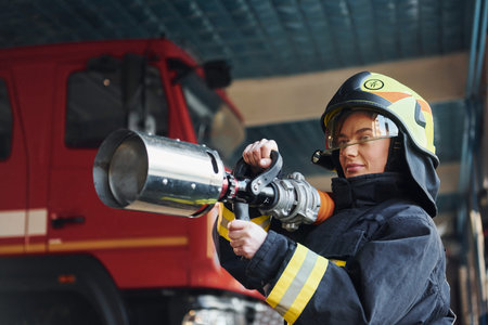 Hose in hands. Female firefighter in protective uniform standing near truck
