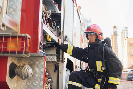 Takes equipment. Female firefighter in protective uniform standing near truck