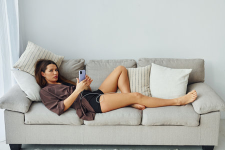 Girl lying down on the bed with smartphone. Interior and design of beautiful modern bedroom at daytimeの写真素材