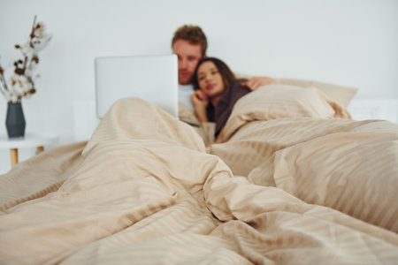 Couple lying down on bed with laptop. Interior and design of beautiful modern bedroom at daytimeの写真素材