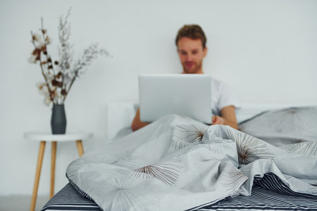 Man lying down on bed with laptop. Interior and design of beautiful modern bedroom at daytimeの写真素材
