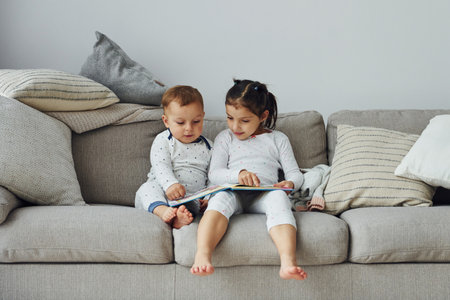 Sister and brother reading book. Interior and design of beautiful modern bedroom at daytimeの写真素材