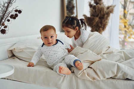 Two kids have fun while liyng down on bed. Interior and design of beautiful modern bedroom at...