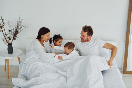 Woman and man lying down on bed with their children. Interior and design of beautiful modern bedroom at daytimeの写真素材