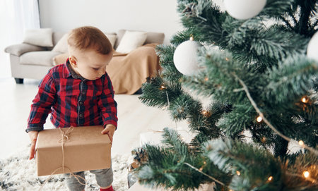 Cute little boy in festive clothes is indoors near christmas tree at New year timeの写真素材